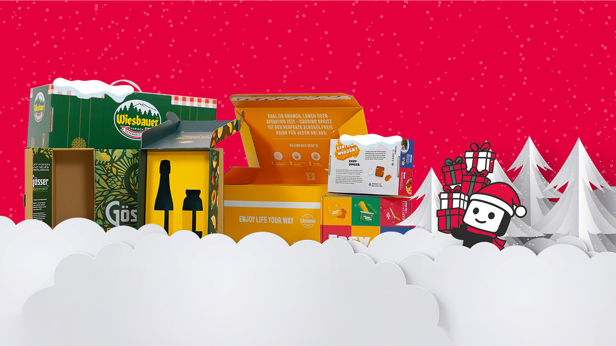 Verschiedene farbige Produktverpackungen weihnachtlich inszeniert mit Schnee, Tannen und Maskottchen mit Geschenken auf rotem Hintergrund.